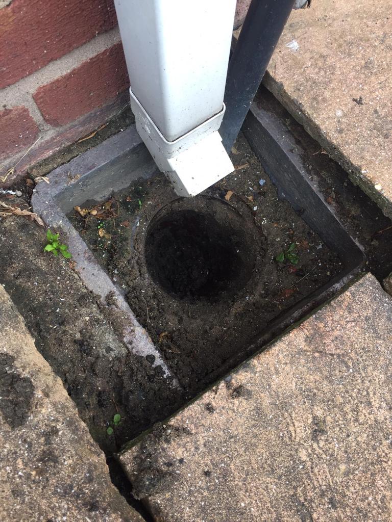 A blocked external drain filled with soil that has been cleared.